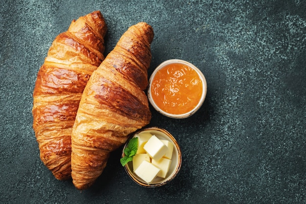 Fresh sweet croissants with butter and orange jam for breakfast.