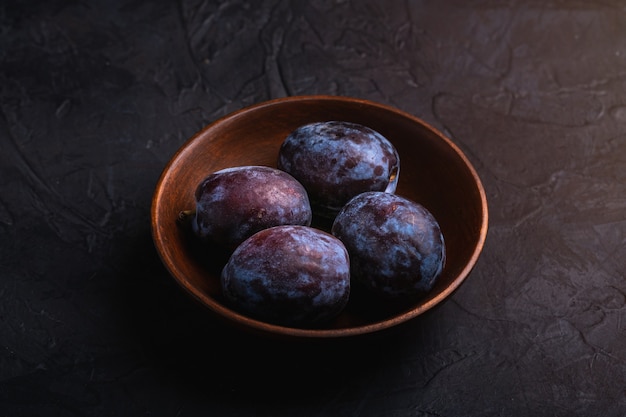 Photo fresh sweet plum fruits in brown wooden bowl, black textured table, angle view