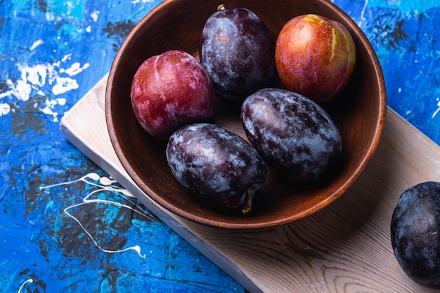 Fresh sweet plum fruits in brown wooden bowl on old cutting board