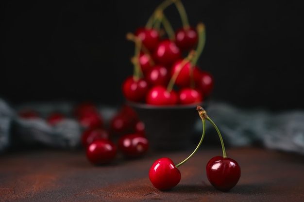 Fresh and sweet red cherries in a black earthenware bowl on a dark surface with water drops