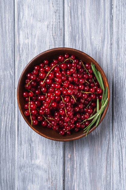 Fresh sweet red currant berries with rosemary leaves in wooden bowl