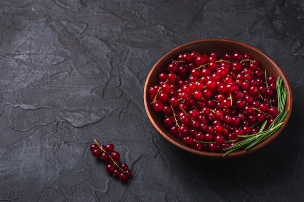 Fresh sweet red currant berries with rosemary leaves in wooden bowl