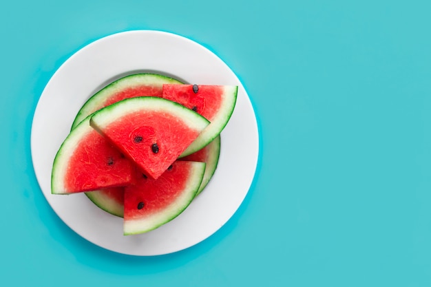 Fresh sweet slices of ripe red watermelon on white plate on blue . Top view, flat lay. Copy space, place for text. Healthy raw food for vegan, vegetarians, summer vacation concept. Cut fruit