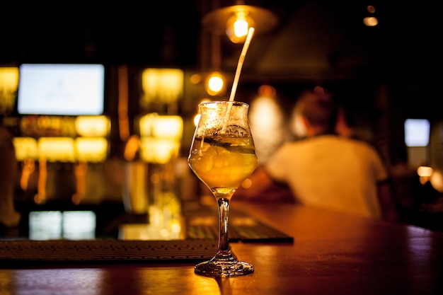 Fresh tall glass of tropical cocktail with juice at bar counter background.