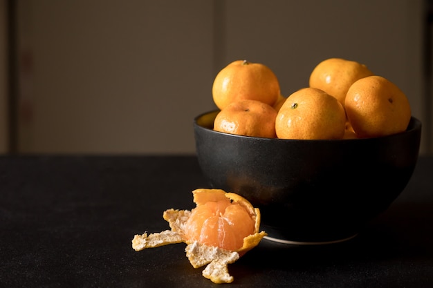 Photo fresh tangerines in bowl, orange fruits on dark background.