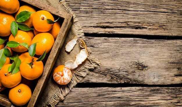 Fresh tangerines in an old box with leaves on wooden table. Top view