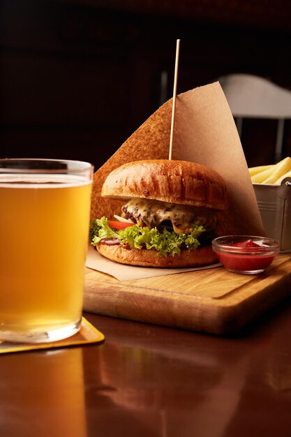 Hamburger di manzo fresco e gustoso con patatine fritte e birra sul tavolo di legno nel pub