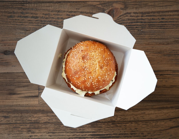 Fresh tasty burger in paper box on wooden table, top view, selective focus