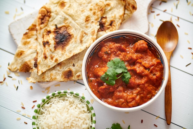 fresh and tasty chicken tikka masala served in ceramic bowl indian spicy curry dish with rice and naan bread on sides close up flat lay