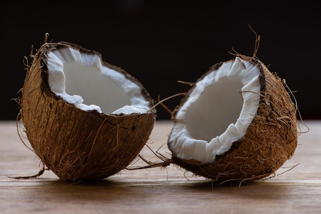 Fresh tasty coconut halves on wooden table isolated on black