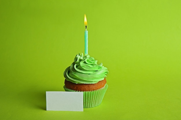Свежий вкусный кекс со свечой и поздравительной открыткой на зеленом фоне