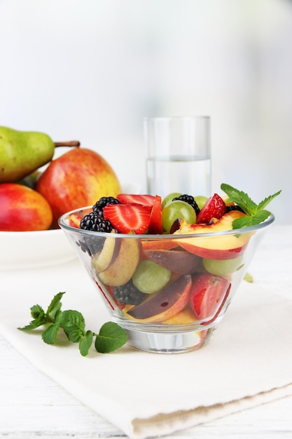 Fresh tasty fruit salad on table on light background