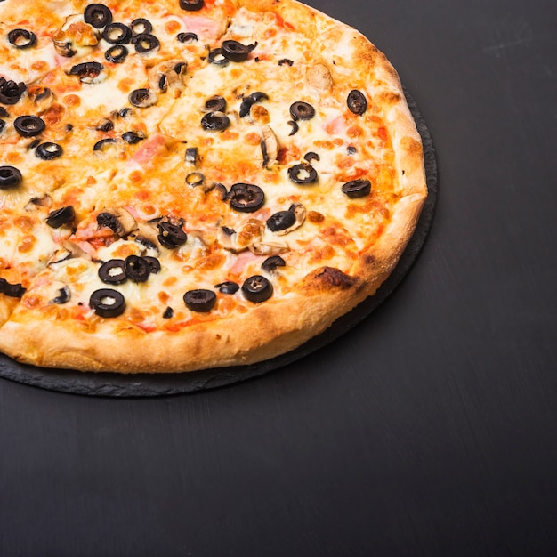 Fresh tasty pizza with olives and meat topping on slate over dark backdrop