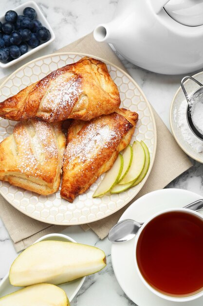 Fresh tasty puff pastry with sugar powder pear blueberries and aromatic tea served on white marble table flat lay