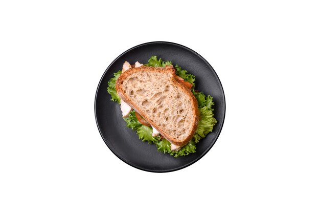 Fresh tasty sandwich with chicken tomatoes and lettuce on a black plate on a dark concrete background