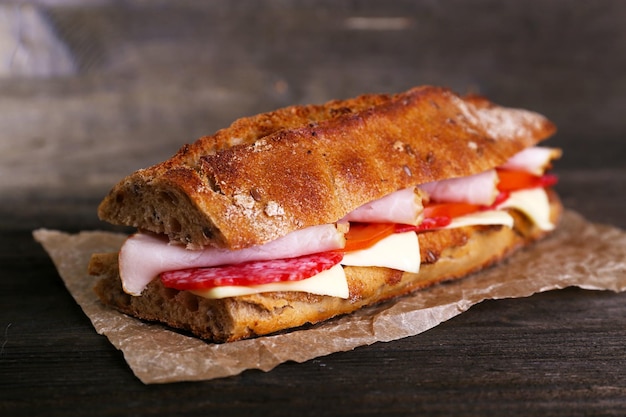 木製の背景の紙にハムとチーズの新鮮でおいしいサンドイッチ