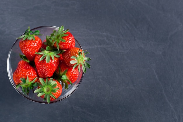 Fresh tasty strawberries in a transparent bowl on a dark gray background