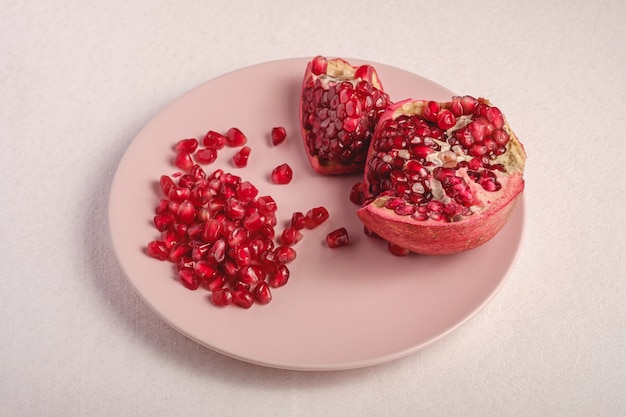 Fresh tasty sweet peeled pomegranate with red seeds in pink plate on white background, angle view, healthy food fruits