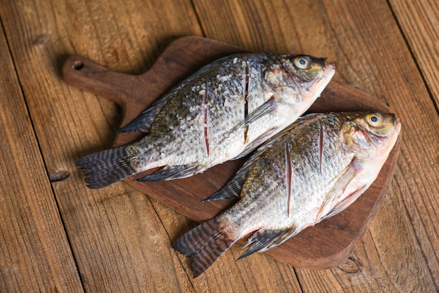 Fresh tilapia fish for cooking food, two raw nile tilapia freshwater fish with salt on wooden wooden board