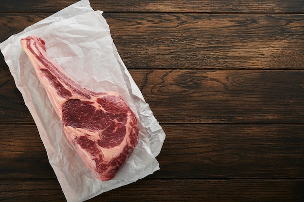 Fresh tomahawk raw steak Dry aged raw tomahawk beef steak with herbs and salt on old wooden background Preparing to grill Top view and copy space