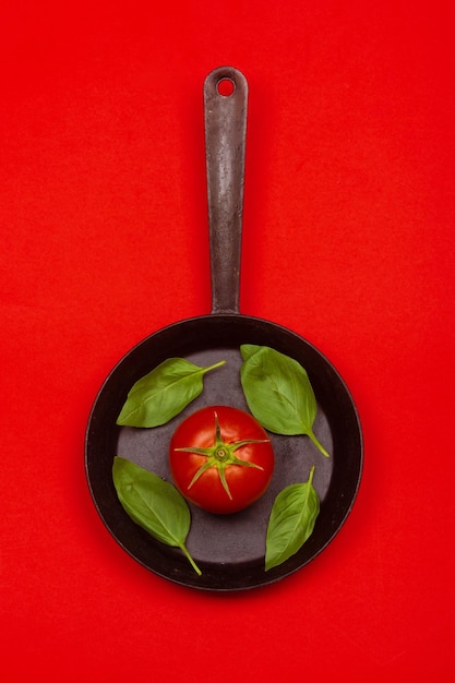 Fresh tomato on frying pan with basilic isolated on red background