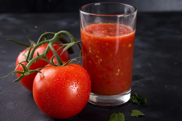 Fresh tomato juice in glass on stone background with water drops on tomatoes. 