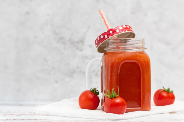 Fresh tomato juice in jar and cherry tomatoes on light.