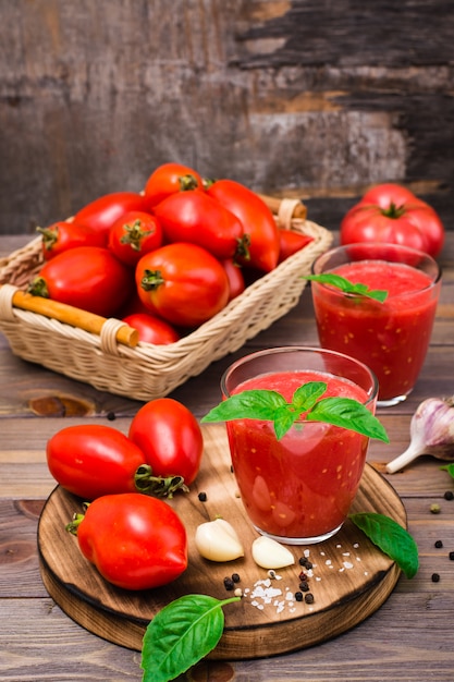 Fresh tomato juice with basil leaves in glasses and ingredients for its preparation on a wooden table