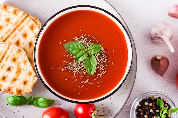 Fresh tomato soup with basil in a bowl and fresh vegetables on the table Top view Closeup