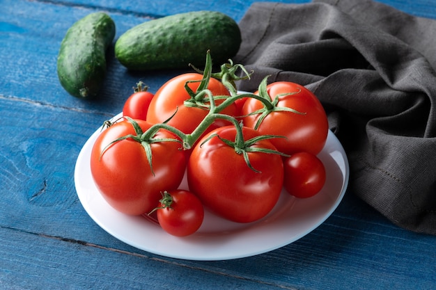 Fresh tomatoes and cucumbers on white plate on wooden