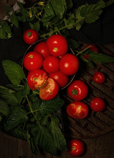 Pomodori freschi sdraiati su un piatto scuro su un tavolo di legno marrone con foglie di pomodoro verdi vista dall'alto