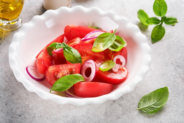 Fresh tomatoes salad with basil leaves olive oil and onion in white bowl on light background Traditional italian or mediterranean food diet Top view