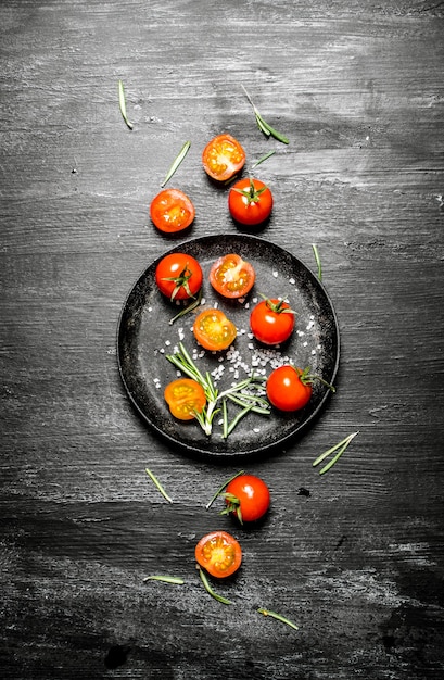 Fresh tomatoes with branches of rosemary. On black rustic background.