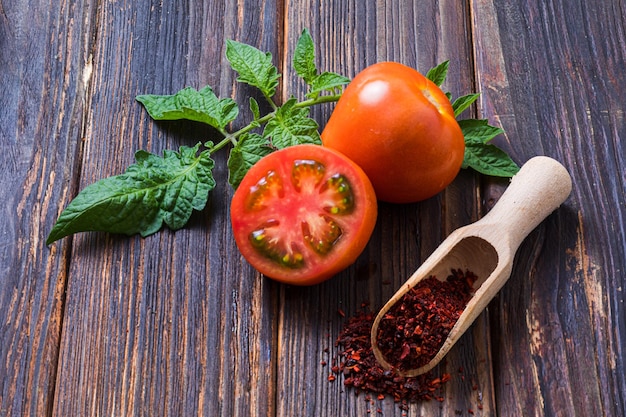 Fresh tomatoes with green leaves placed near wooden scoop with tomato seasing Using organic vegeables for preparing tasty condiments Healthy cuisine concept