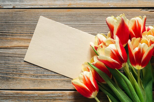 Foto tulipi freschi e un pezzo di carta su sfondo di legno con spazio per il testo