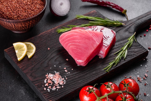 Fresh tuna fillet steaks with spices and herbs on a black background