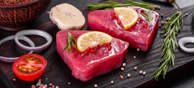 Fresh tuna fillet steaks with spices and herbs on a black background