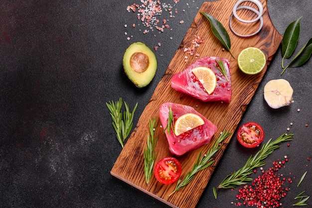 Fresh tuna fillet steaks with spices and herbs on a black surface