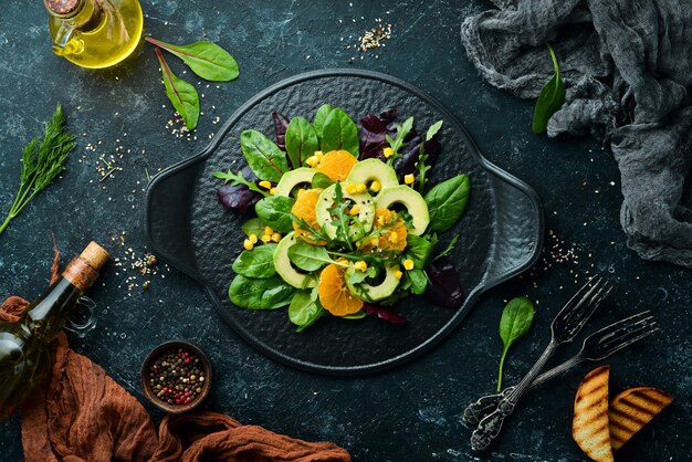 Fresh vegan avocado salad with oranges and spinach on a black plate Rustic style Top view Free space for your text