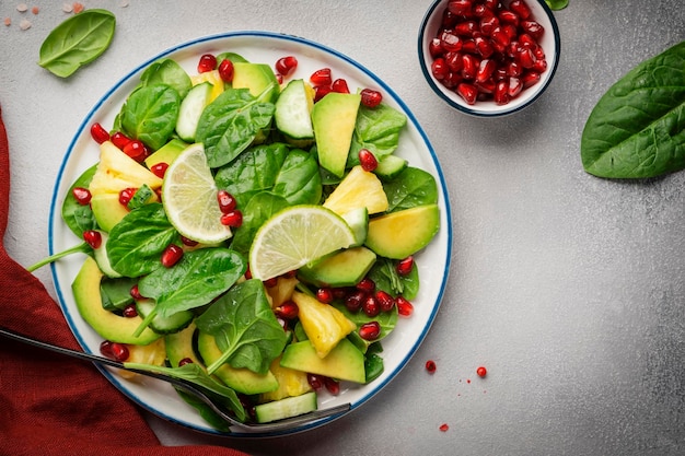 Fresh vegan salad with pineapple spinach avocado and pomegranate seeds gray kitchen table top view Healthy eating clean food diet weight loss concept