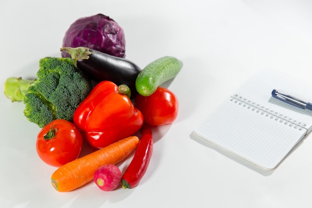 Fresh vegetable collection and notebook with diet plan isolated on white background