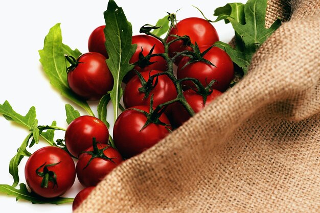 白い背景のコピースペースに分離された黄麻布の袋の新鮮な野菜緑ルッコラチェリートマトの赤い色