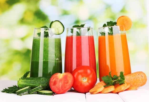 Fresh vegetable juices on wooden table on green background