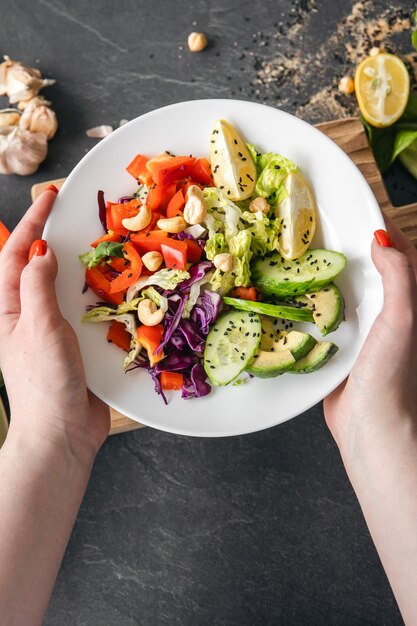 Foto insalata di verdure fresche nelle mani delle donne sullo sfondo di un tavolo scuro