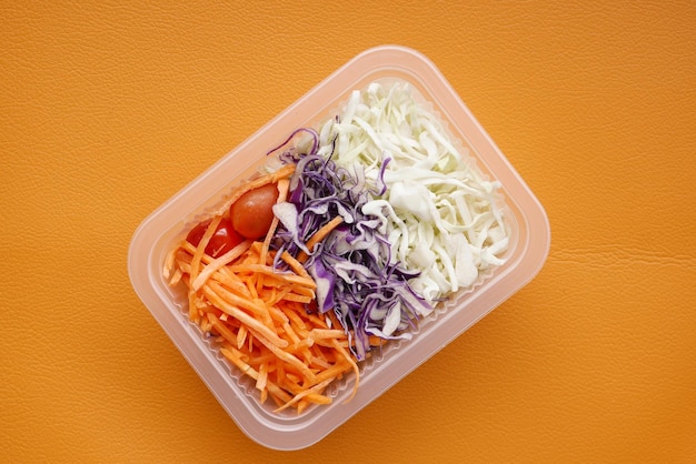Салат из свежих овощей в пластиковом контейнере на оранжевом фоне
