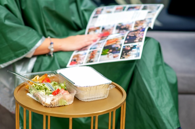 Fresh vegetable salad on the table during young woman reading magazine in beauty salon.