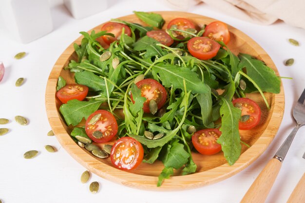 신선한 야채 샐러드. 나무 접시에 arugula, 체리 토마토와 호박 씨앗의 채식 샐러드. 순수하고 자연적인 음식의 개념. 가로 사진.