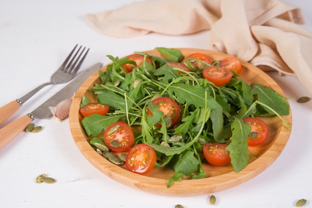 신선한 야채 샐러드. 나무 접시에 arugula, 체리 토마토와 호박 씨앗의 채식 샐러드. 순수하고 자연적인 음식의 개념. 가로 사진.