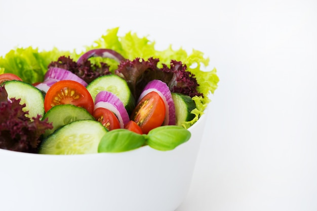 白い背景の上の新鮮野菜のサラダを閉じます。レタス、トマト、玉ねぎ、きゅうりのディナー。