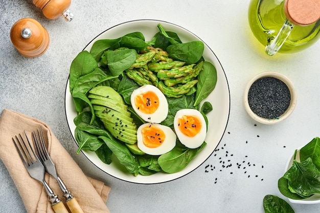 Fresh vegetable salad with avocado, asparagus, boiled eggs on light concrete surface. Top view.